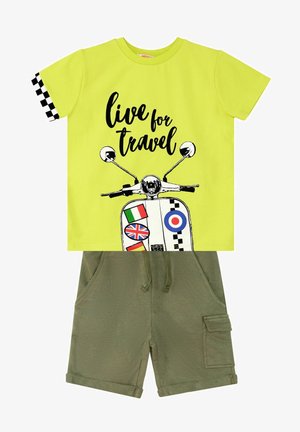 T-shirt verde lime con testo grafico nero e design di uno scooter; abbinata a pantaloni corti verde oliva con tasche laterali e orli arrotolati.