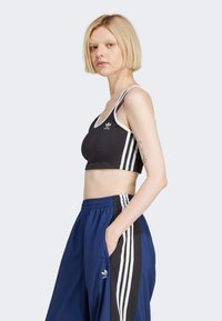 Zwarte cropped sport-bh met witte accenten en drie strepen aan de zijkanten, gecombineerd met blauwe trainingsbroek met zwarte zijstrepen.