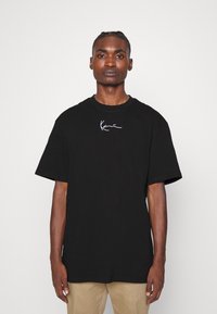 Black cotton t-shirt with a crew neck and short sleeves. Features a white logo on the left chest. Fabric appears smooth and lightweight.