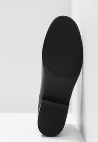 Suola di scarpa in pelle nera con una finitura texturizzata. Presenta un'accento marrone chiaro vicino al tallone. Marcata con "MICHAEL KORS" e dettagli della taglia.