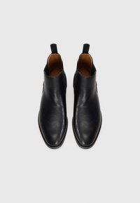 Botines de cuero negro con una textura suave, punta afilada, paneles laterales elásticos y una lengüeta para facilitar su uso.