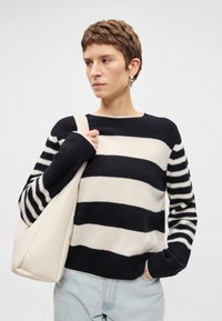 Sweater listrado em preto e branco com mangas longas, apresentando um pescoço redondo e punhos canelados; combinado com uma mala tote em cor creme.