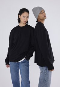 Cămăși negre cu mânecă lungă, asociate cu blugi albaștri; un model poartă o căciulă tricotată gri. Design simplu, croi lejer și textură moale.