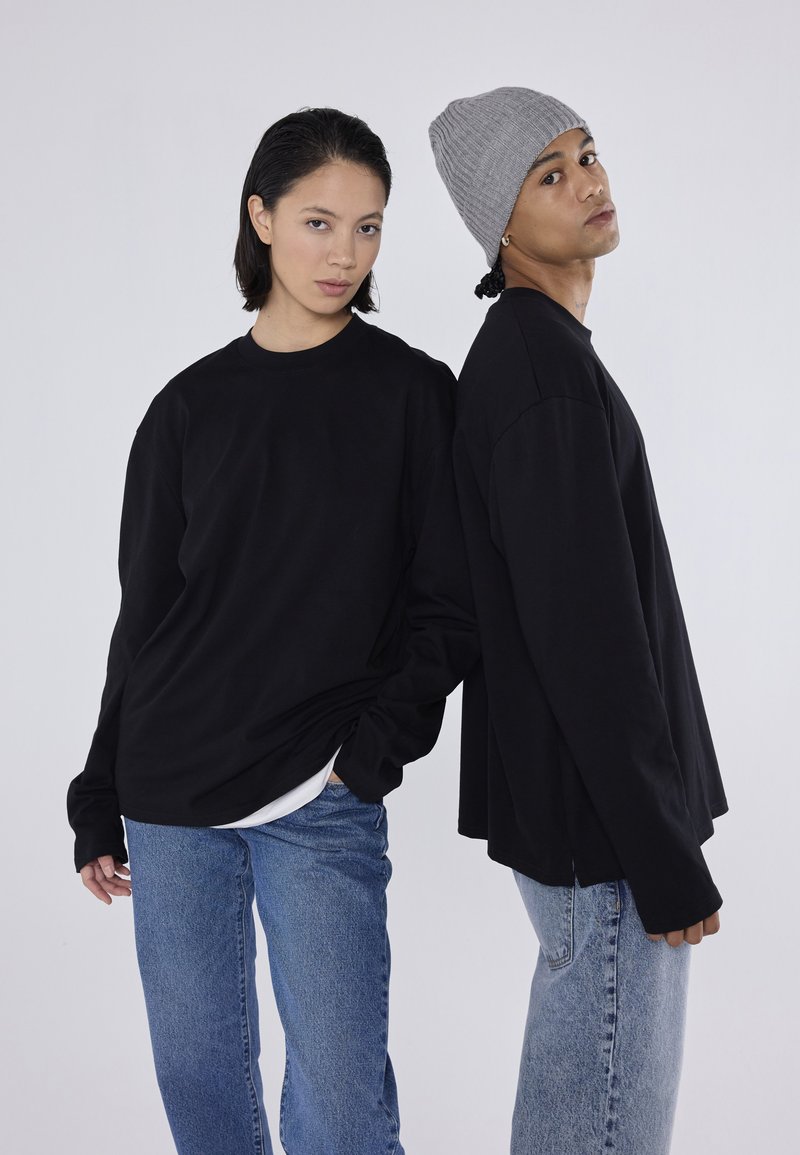 Cămăși negre cu mânecă lungă, asociate cu blugi albaștri; un model poartă o căciulă tricotată gri. Design simplu, croi lejer și textură moale.