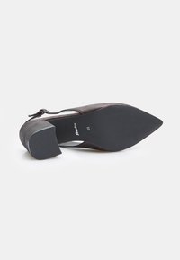 Scarpa con tacco a cuneo in suede nero, con punta affusolata e design aperto ai lati. Suola in gomma nera con texture, caratterizzata da una parte superiore liscia con un leggero lucido.