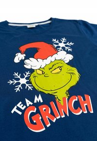 T-shirt di cotone blu navy con un personaggio cartone animato verde che indossa un cappello di Babbo Natale, fiocchi di neve e la scritta "TEAM GRINCH" in rosso e bianco.