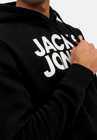 Schwarzer Hoodie mit weißem "JACK & JONES"-Druck. Verfügt über eine Kapuze mit Kordelzug und gerippte Bündchen. Der Stoff wirkt weich und strukturiert.