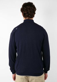 Pull-over bleu marine à manches longues, col haut, poignets et ourlet côtelés. Texture lisse et détail de logo subtil sur l'épaule.