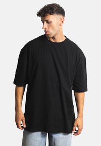 Černé oversized tričko s krátkým rukávem, kulatým výstřihem a měkkou texturou, kombinované se světle modrými džínami.