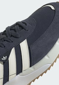 Marinblå sneaker med ovandel i mocka och tyg, med tre vita ränder, texturerade detaljer och en gummisula med mönster för bra grepp.