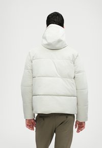 Casaco puffer de cor clara com um padrão texturizado, apresentando um capuz e design acolchoado. A vista traseira mostra uma silhueta cropped e punhos elásticos.