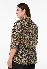 Chemise à imprimé léopard avec une coupe décontractée, dotée de manches courtes repliées, d'un col et d'un tissu léger dans des teintes de beige et de noir.