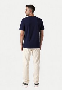 Mørkeblå kortærmet T-shirt med rund hals, parret med cremefarvede bukser og grå sneakers, set fra ryggen.