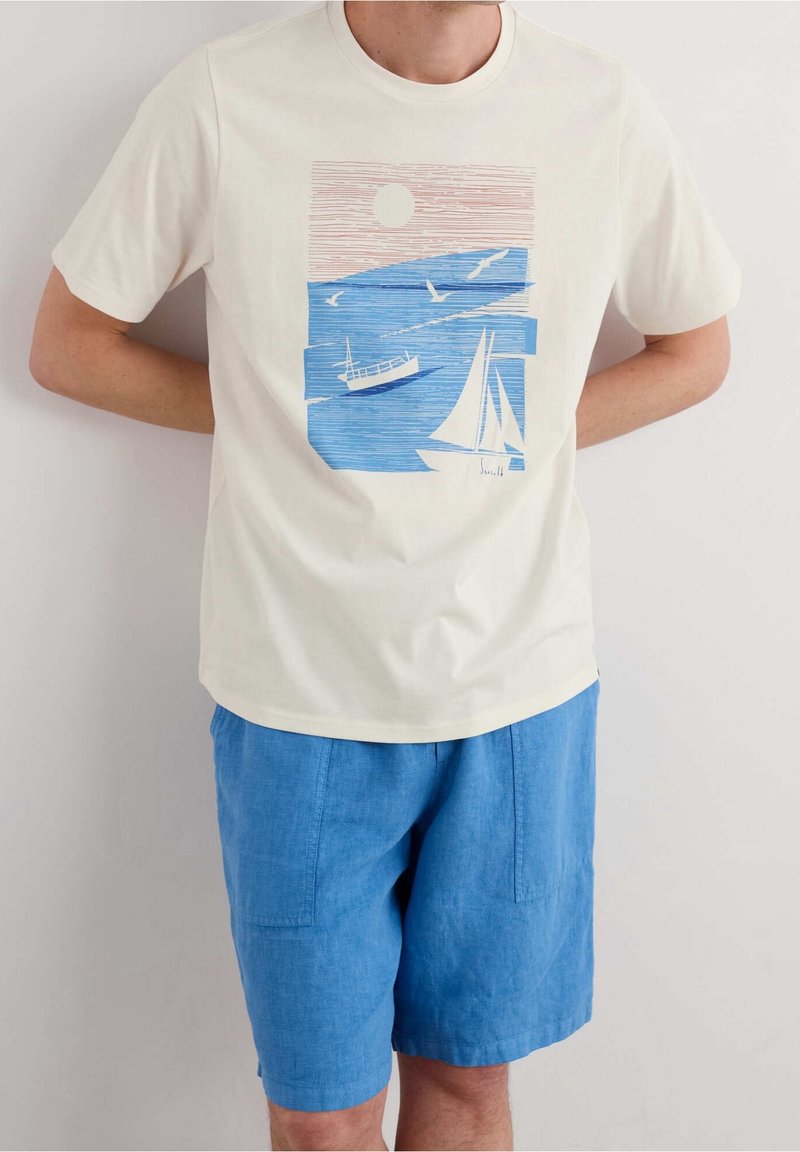 T-shirt en coton crème avec une illustration maritime colorée mettant en scène des bateaux et des oiseaux, associé à des shorts en lin bleu clair avec poches.