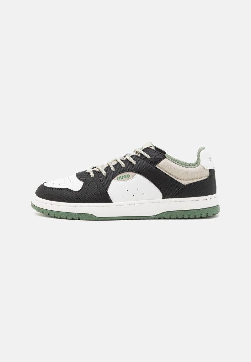 Svart og hvit sneaker med grønne detaljer, med en teksturert overdel, rund tå og flate lisser. Merkevarelogo på siden og hælen.