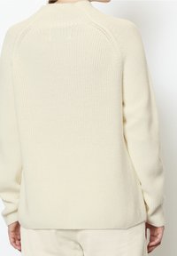 Pull couleur crème avec un motif en tricot texturé, col montant et épaules tombantes. Tissu lisse avec une coupe décontractée.