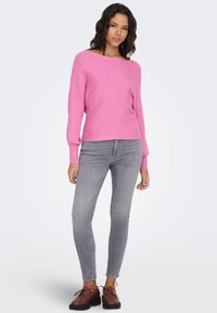 Maglione rosa a coste in maglia, taglio ampio con maniche lunghe, abbinato a jeans skinny grigio chiaro e scarpe marroni con lacci. Design semplice.