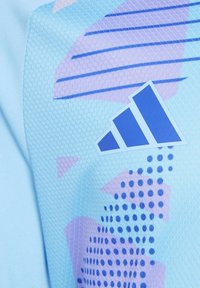 Lichtblauw sportshirt met geometrische paarse en blauwe patronen. Gelaagd textiel met hexagonale details. Adidas-logo zichtbaar.