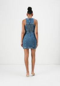 Robe mini en denim avec une silhouette ajustée, des bretelles réglables et un dos smocké. Couleur bleu clair avec une texture lisse.