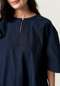 Navy blue cotton tunic with a round neckline, button closure at the neck, and short sleeves. Features a stitched front panel design.