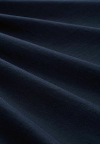 Jūras zila kokvilnas audums, kas izvietots mīkstos, gludos locījumos, demonstrējot vienmērīgu tekstūru bez rakstiem vai detaļām.