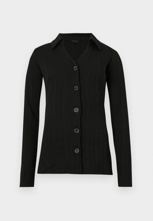 Chemise noire à manches longues avec une texture côtelée, boutonnée sur le devant, et un col pointu. Elle comporte six boutons ronds le long de la patte de boutonnage.