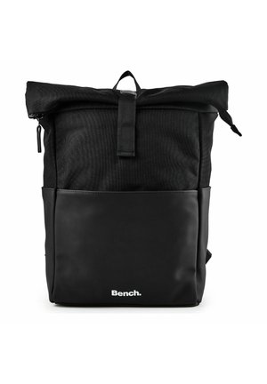 Mochila negra con cierre enrollable, bolsillo frontal con cremallera y logo "Bench." en el panel inferior frontal sobre fondo blanco.
