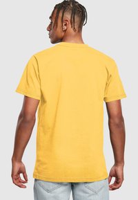 Apsidinis vaizdas trumpomis rankovėmis, apvalia iškirpte t-shirt ryškiai geltonos spalvos, pagamintas iš medvilnės, su laisvu siluetu ir subtiliais siūlės detalėmis.
