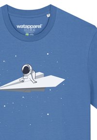 T-shirt en coton bleu à manches courtes avec un graphique d'astronaute blanc assis sur un avion en papier, avec de petites étoiles en arrière-plan.