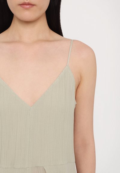 Light green, pleated fabric top with a deep V-neckline and thin straps, showing soft texture and layered design.