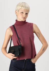 Burgundi värvi seljatuuleta turtleneck top, millel on ribakujuline kaelus, kombineeritud musta kotiga üle õla, millel on ristküliku kujuline klapp ja õlarihm.