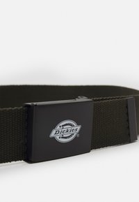 Cinto de tecido cáqui com um fecho de metal preto apresentando o logo "Dickies". O cinto tem um padrão texturizado e uma forma retangular.