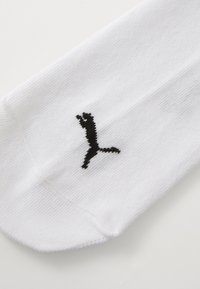 Calcetín de algodón blanco con un diseño de logo negro. La tela tiene una textura suave y un puño acanalado, sin patrones ni acentos adicionales.