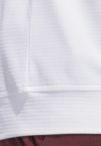 Valkoinen, teksturoitu kangas, jossa on ribbineulospinta ja sileä helmaviiste. Vaate on kerrostettu viininpunaisen, kuvioidun materiaalin päälle.