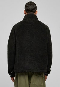 Giacca in pile nera con colletto alto e tessuto testurizzato, caratterizzata da una vestibilità rilassata e un orlo che si ferma in vita.