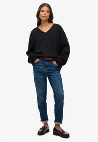 Czarny sweter z dzianiny w serek, zestawiony z niebieskimi dżinsami. Brązowy pleciony pasek i ciemne mokasyny dopełniają stylizację. Casualowy, luźny fason.