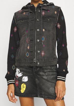 Schwarze Denimweste und Hoodie mit bunter Stickerei kombiniert mit einem schwarzen Denimrock mit Mickey-Maus-Grafik.