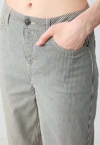 Pantaloni a righe in bianco e nero, con vita aderente, tasca frontale e chiusura con bottone in metallo. La trama del tessuto è liscia con righe verticali.