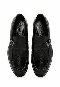 Zwarte leren schoenen met een gestructureerd oppervlak, voorzien van een platte zool, gladde accenten en een gespsluiting op de band.