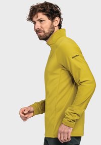 Gelber langärmeliger Pullover mit hohem Kragen, der über eine Strukturierung und ein dezentes Logo am Ärmel verfügt. Figurbetonte Passform mit Akzenten an den Bündchen.