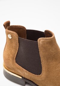 Stivale Chelsea in suede marrone con pannello laterale elastico nero, linguetta sul retro e tacco della suola nera con accenti dorati.