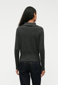 Mørkegrå strikket genser med brettet krage, tettsittende ermer og ribbestrikket søm, kombinert med mørke denimjeans. Jevn tekstur, enkelt design.