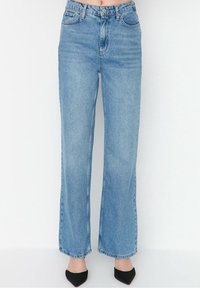 Jeans de mezclilla anchos de color azul claro con una cintura alta, que cuentan con un cierre de botón, bolsillos frontales y una textura suave, ligeramente desvaída.