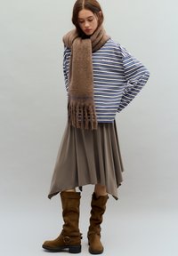 Bluză cu mâneci lungi cu dungi, eșarfă bej și fustă maro asimetrică, asortate cu cizme maro din piele întoarsă până la genunchi, cu catarame.