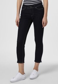 Mörktvättade jeans till anklarna med en åtsittande siluett, synlig sömnad och rå kant, i kombination med vita sneakers.