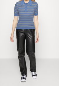 Blårandig polo skjorta med korta ärmar, ribbad textur, i kombination med svarta läderbyxor och svartvita sneakers.
