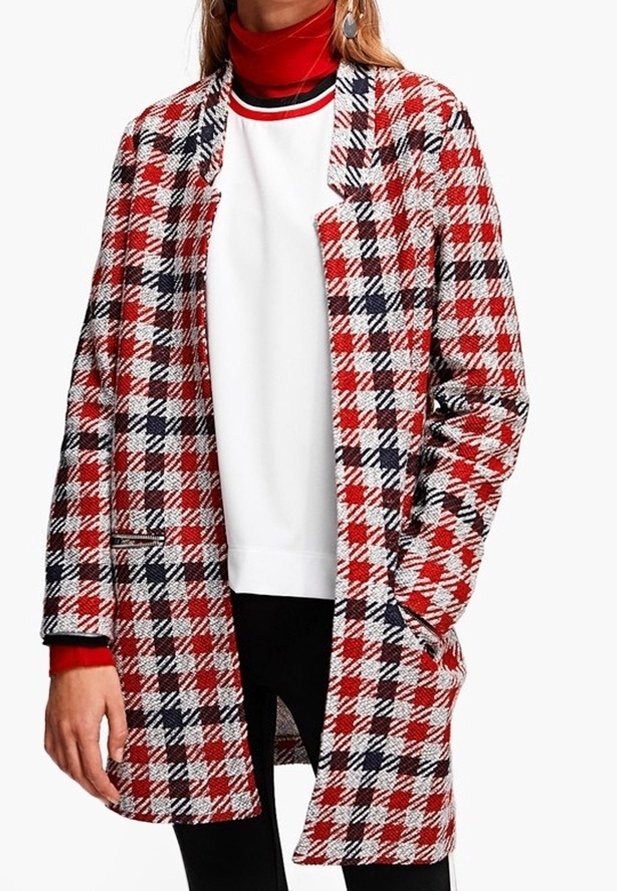 Kvinde iført en rød, hvid og sort ternet frakke over en hvid sweatshirt med rød og sort kant, kombineret med sorte bukser.