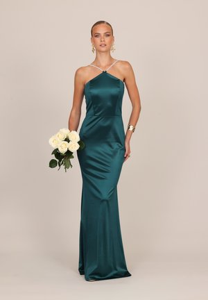 Femme portant une robe en satin sarcelle à col licou, tenant un bouquet de roses blanches, accessoirisée avec des boucles d'oreilles en or et un bracelet manchette.