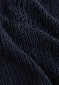 Tissu bleu marine foncé avec des nervures texturées verticales et des plis doux créant un motif ondulé et de la profondeur.