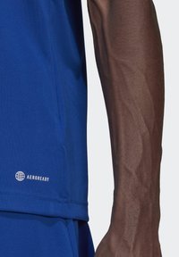 Royal blå athletic skjorte laget av glatt, lett stoff med mesh-detaljer. Har "AEROREADY" logo nær sømmen.